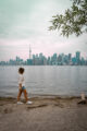 A woman walking along the sandy shore of the Toronto Islands with the Toronto city skyline in the background.