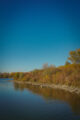 Rive d'un lac à Toronto ornée de buissons et d'arbres aux couleurs d'automne rouges et jaunes, avec le reflet dans l'eau sous un ciel bleu clair, un spot photo accessible sans voiture