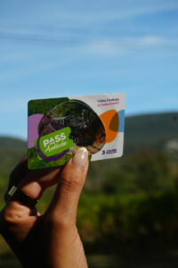 Main tenant la carte Pass Ardèche 3 jours devant un paysage naturel sous un ciel bleu.